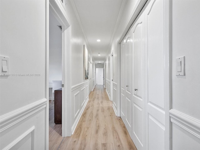 hallway with light wood finished floors, recessed lighting, wainscoting, crown molding, and a decorative wall