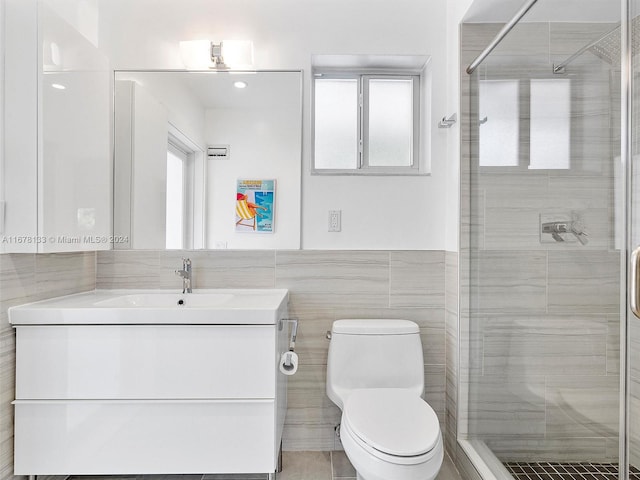 bathroom featuring a shower with door, vanity, toilet, and tile walls