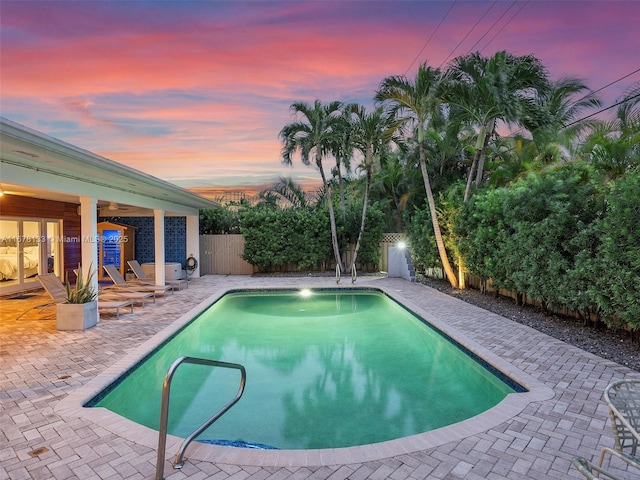 pool at dusk with an outdoor pool, a patio, a fenced backyard, and a ceiling fan