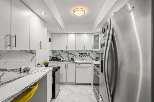 kitchen with light stone countertops, appliances with stainless steel finishes, sink, backsplash, and white cabinets