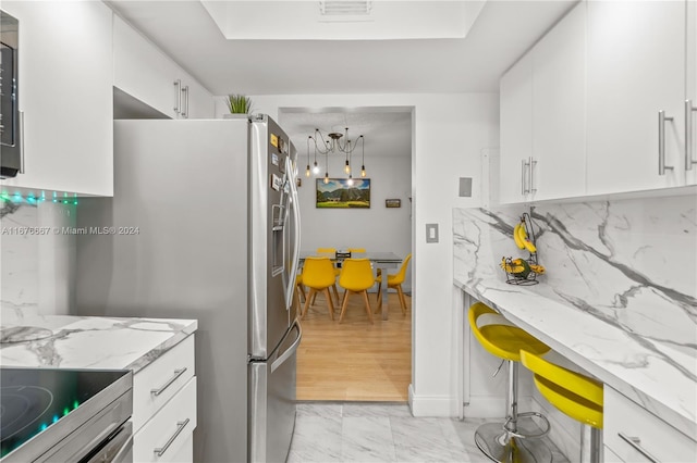 kitchen featuring stainless steel appliances, backsplash, light stone countertops, white cabinetry, and light hardwood / wood-style floors