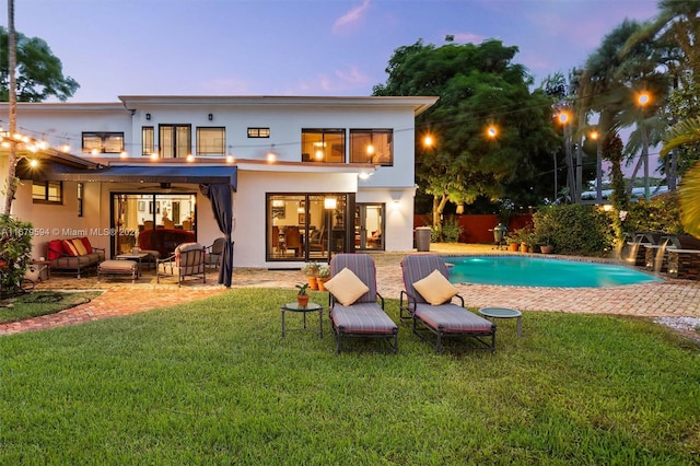 back house at dusk with a patio area, a fenced in pool, an outdoor hangout area, and a lawn