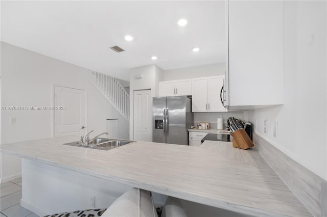 kitchen with range, kitchen peninsula, white cabinetry, light tile patterned floors, and stainless steel refrigerator with ice dispenser