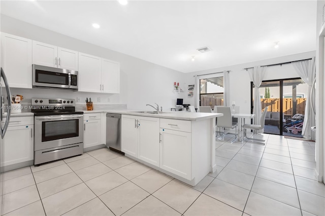 kitchen with light tile patterned flooring, sink, kitchen peninsula, stainless steel appliances, and white cabinets