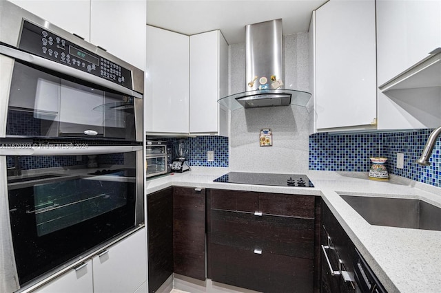 kitchen featuring wall chimney exhaust hood, white cabinetry, black electric cooktop, and stainless steel double oven