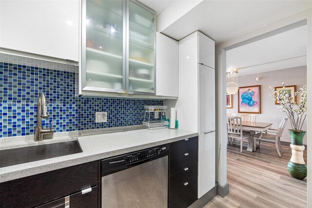 kitchen with tasteful backsplash, sink, stainless steel dishwasher, white cabinets, and light hardwood / wood-style flooring