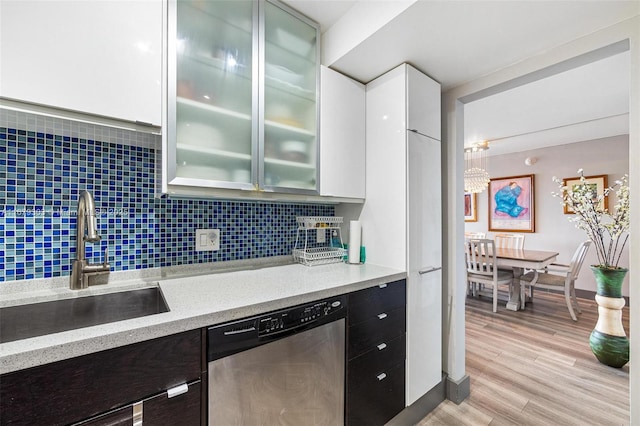 kitchen with white cabinets, glass insert cabinets, light countertops, stainless steel dishwasher, and a sink