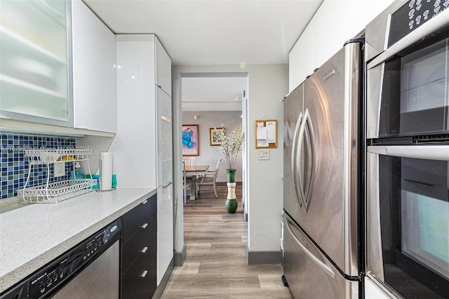 kitchen featuring backsplash, stainless steel appliances, light wood-type flooring, and white cabinets