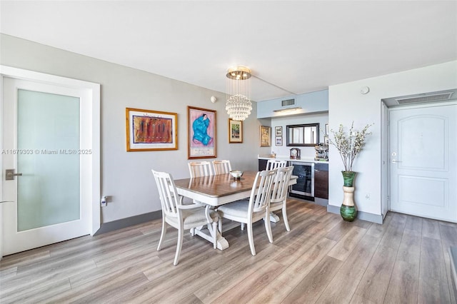 dining space with wine cooler, baseboards, light wood finished floors, and an inviting chandelier