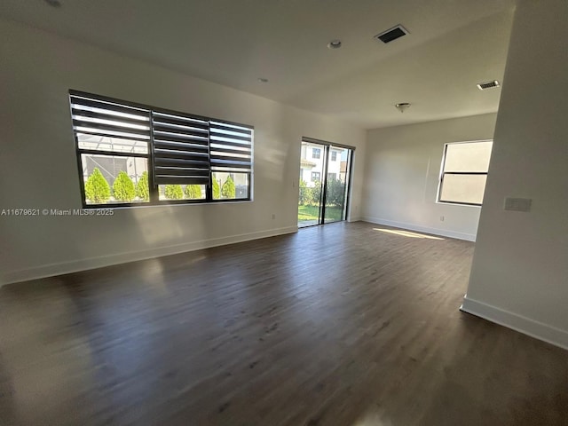 unfurnished room with visible vents, dark wood finished floors, and baseboards