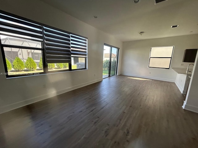 unfurnished living room with dark wood-type flooring, visible vents, and baseboards