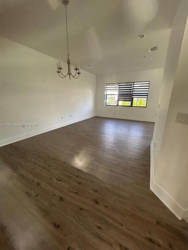 unfurnished dining area featuring a notable chandelier, visible vents, baseboards, and dark wood-type flooring