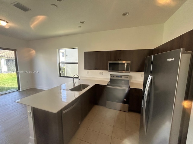 kitchen featuring a peninsula, stainless steel appliances, dark brown cabinets, light countertops, and a sink