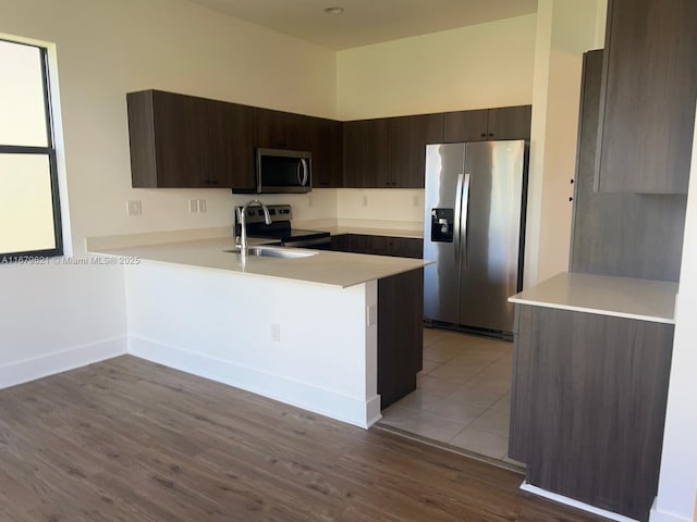 kitchen featuring stainless steel appliances, light countertops, a peninsula, and dark brown cabinets