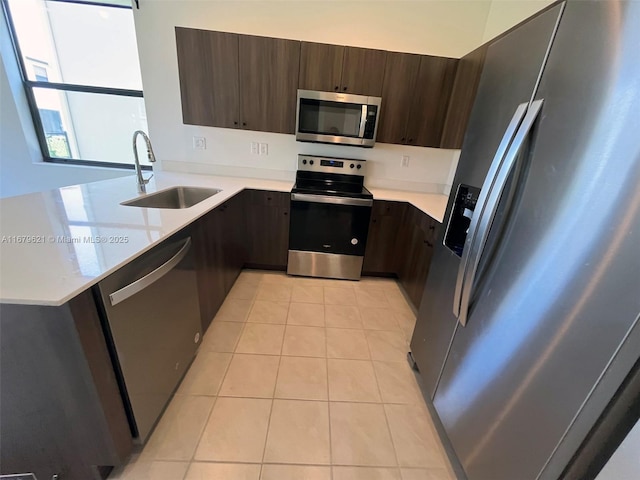 kitchen featuring dark brown cabinetry, light tile patterned floors, appliances with stainless steel finishes, light countertops, and a sink