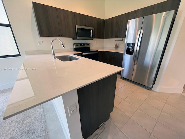 kitchen featuring stainless steel appliances, light countertops, a sink, dark brown cabinetry, and a peninsula