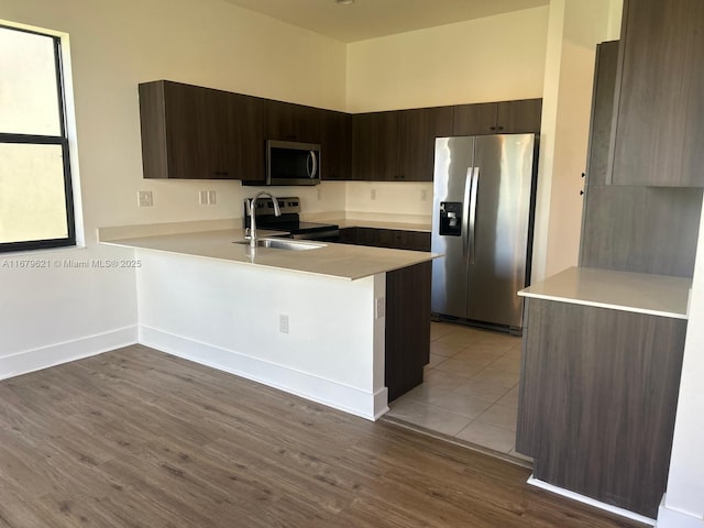 kitchen featuring stainless steel appliances, a peninsula, light countertops, and dark brown cabinetry