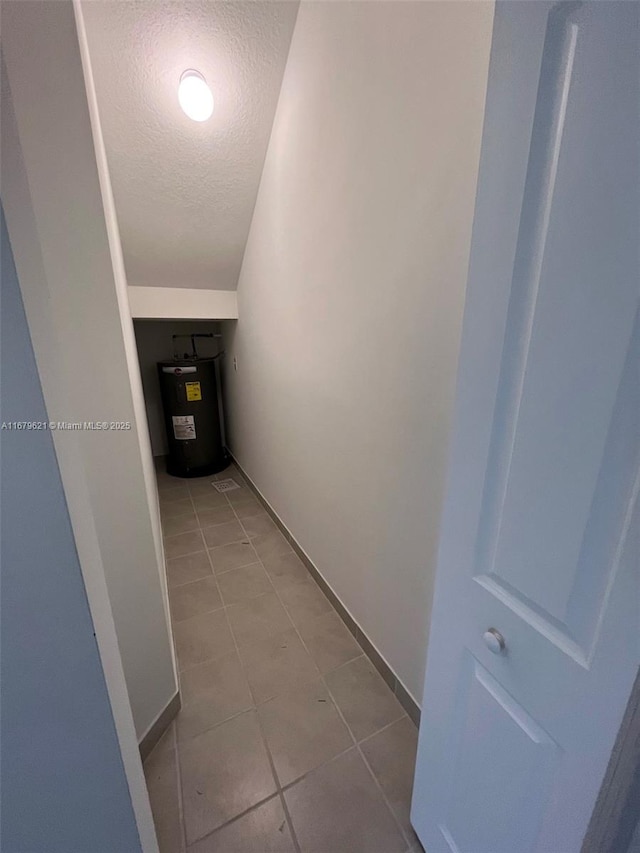 hall with light tile patterned floors, baseboards, a textured ceiling, and electric water heater