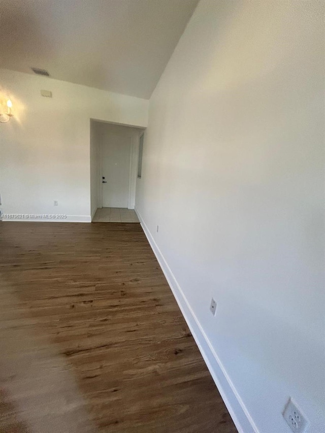 empty room with lofted ceiling, visible vents, baseboards, and dark wood finished floors