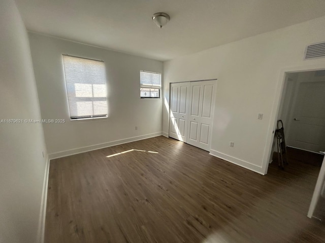 unfurnished bedroom with a closet, visible vents, dark wood finished floors, and baseboards