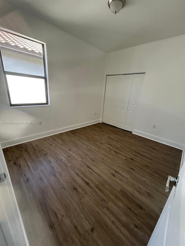 unfurnished bedroom with a closet, baseboards, and dark wood-type flooring