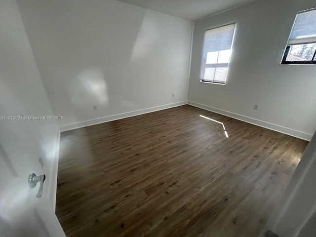 spare room with plenty of natural light, baseboards, and dark wood-type flooring