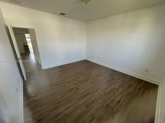 unfurnished room featuring dark wood-style flooring, visible vents, and baseboards