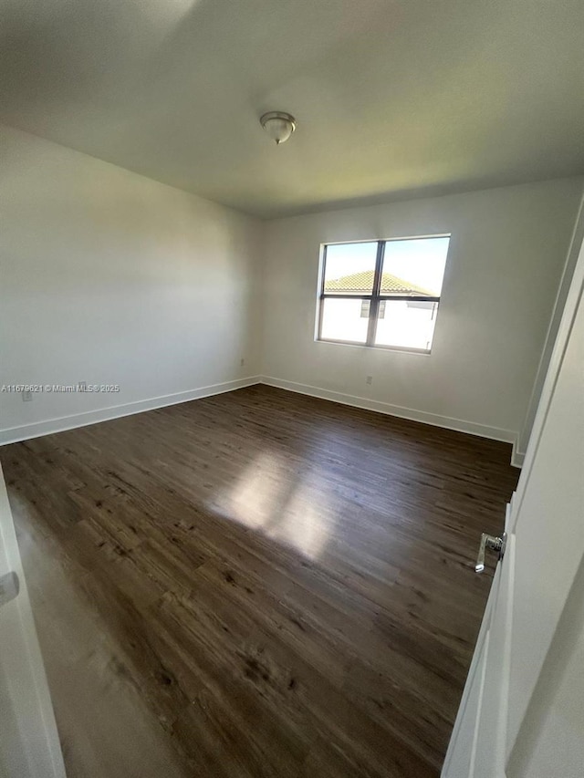 spare room with dark wood-style flooring and baseboards