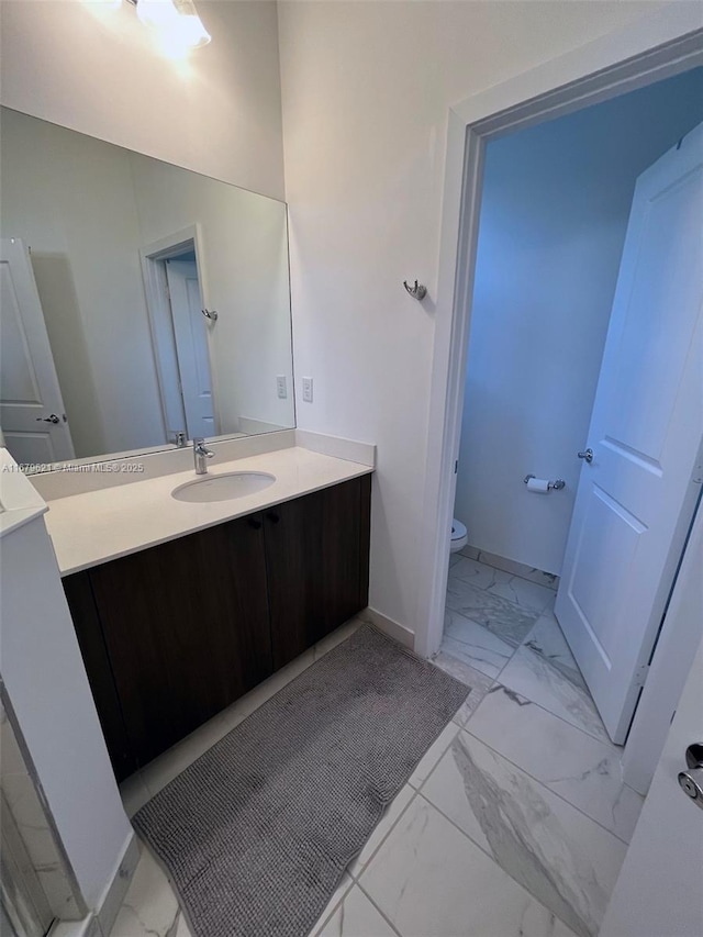 bathroom with marble finish floor, vanity, toilet, and baseboards