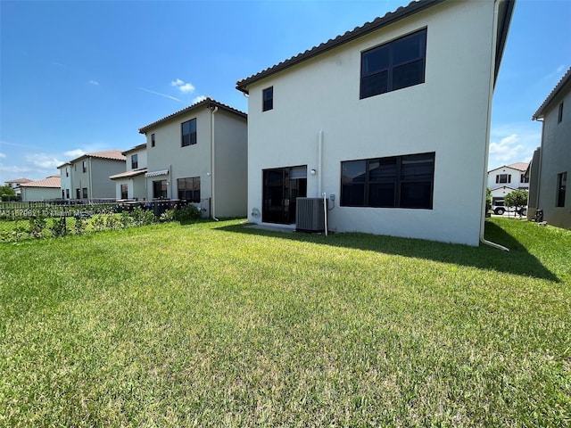 rear view of house with cooling unit, a yard, fence, and stucco siding