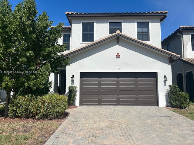 view of front of house featuring an attached garage, a tiled roof, decorative driveway, and stucco siding