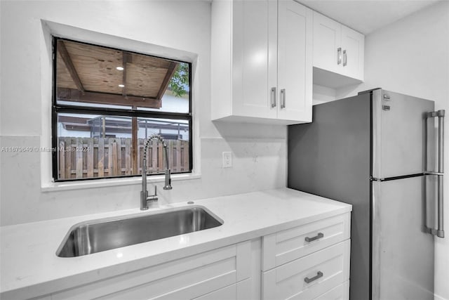 kitchen with white cabinetry, light stone counters, stainless steel refrigerator, and sink