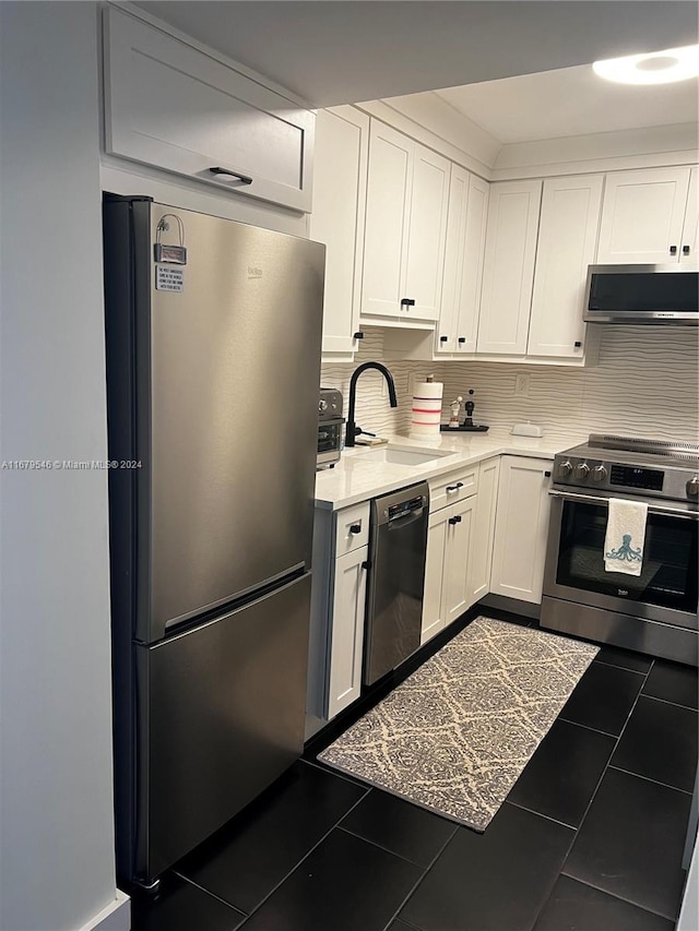 kitchen with backsplash, appliances with stainless steel finishes, white cabinetry, dark tile patterned flooring, and sink