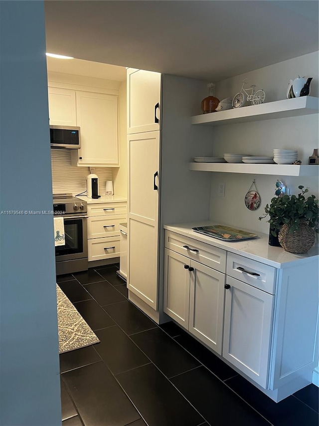 kitchen featuring decorative backsplash, appliances with stainless steel finishes, white cabinets, and dark tile patterned flooring