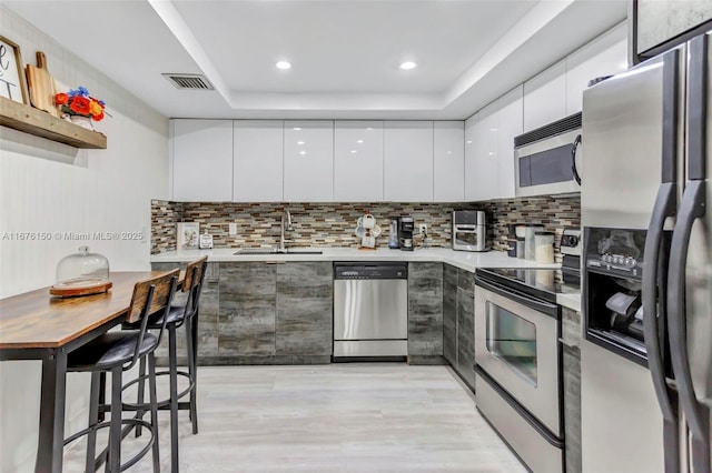 kitchen with sink, stainless steel appliances, tasteful backsplash, a raised ceiling, and white cabinets