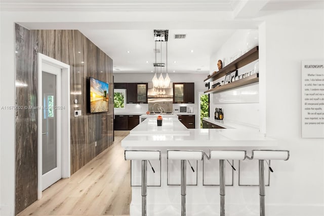 kitchen featuring a kitchen breakfast bar, light hardwood / wood-style flooring, hanging light fixtures, kitchen peninsula, and dark brown cabinets