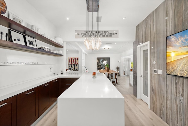 kitchen with a notable chandelier, a kitchen island, light wood-type flooring, and pendant lighting