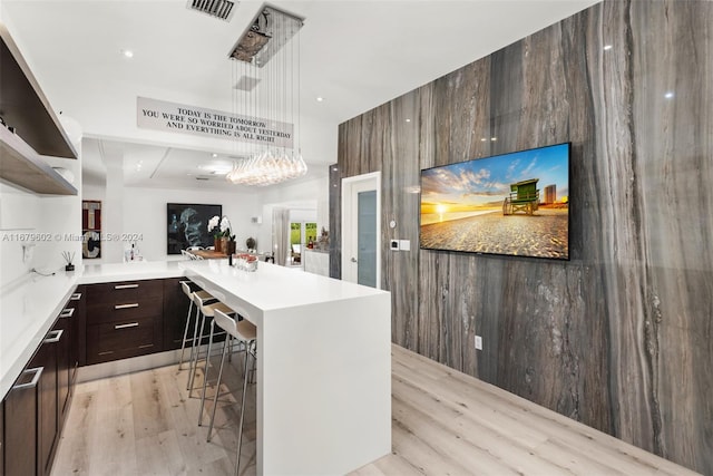 kitchen featuring a kitchen island, hanging light fixtures, light hardwood / wood-style floors, a notable chandelier, and a breakfast bar area