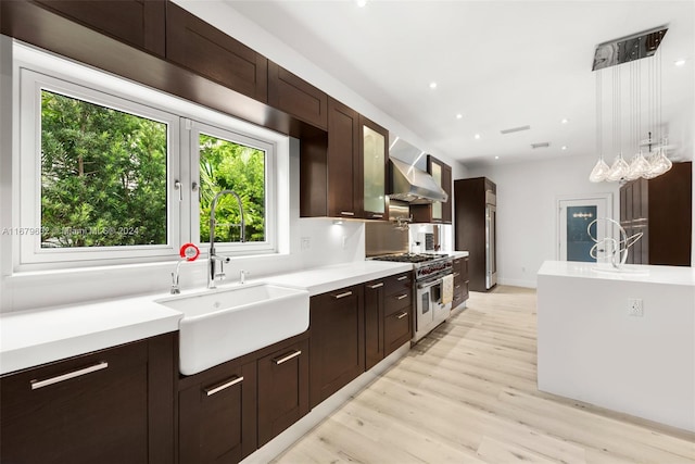 kitchen featuring wall chimney range hood, sink, light wood-type flooring, pendant lighting, and double oven range