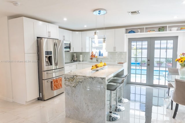 kitchen featuring appliances with stainless steel finishes, white cabinetry, decorative light fixtures, and plenty of natural light