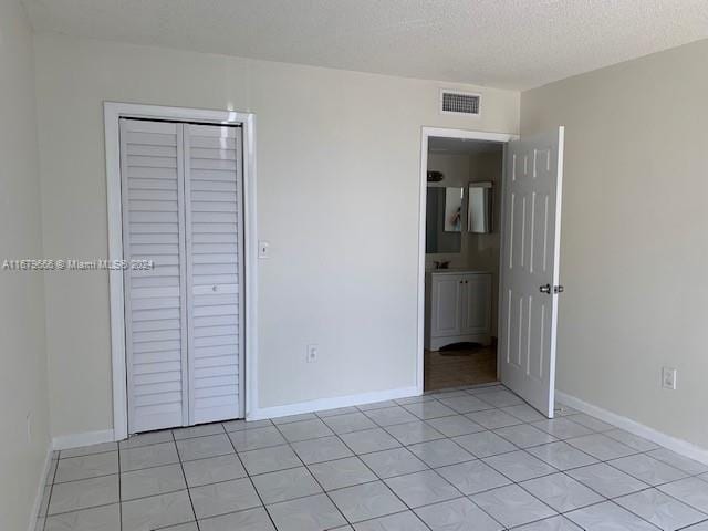 unfurnished bedroom featuring light tile patterned flooring, baseboards, a closet, and a textured ceiling