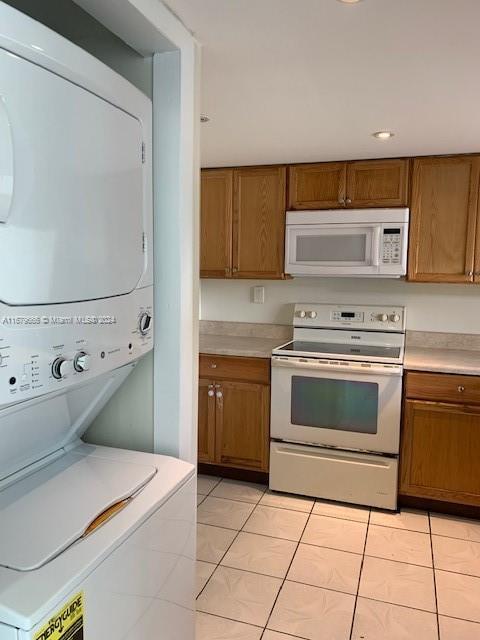 kitchen featuring white appliances, stacked washer / dryer, brown cabinets, light tile patterned floors, and light countertops