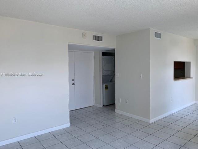 tiled empty room with stacked washer and dryer and a textured ceiling