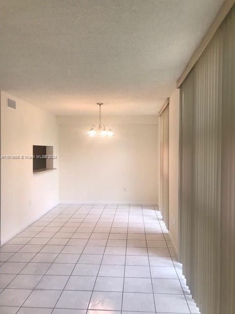 empty room featuring a chandelier, light tile patterned floors, and a textured ceiling