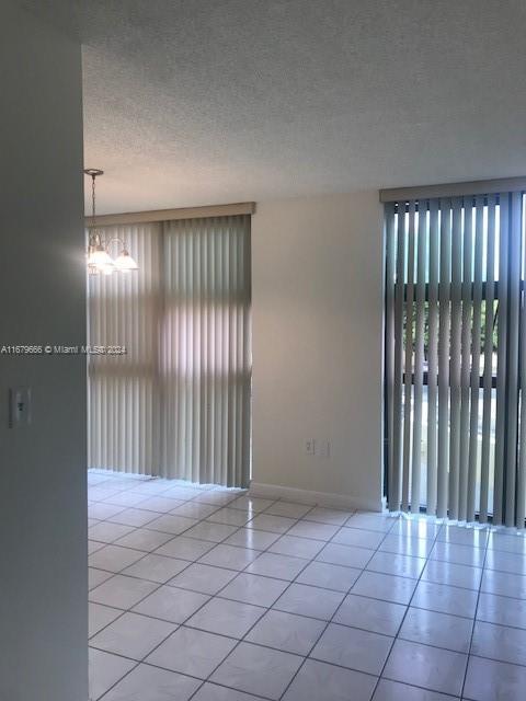 tiled empty room with plenty of natural light, baseboards, and a textured ceiling