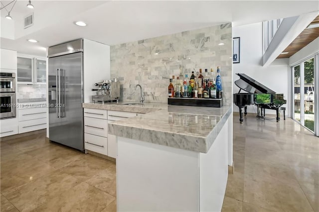 kitchen with tasteful backsplash, light stone countertops, sink, stainless steel appliances, and white cabinets