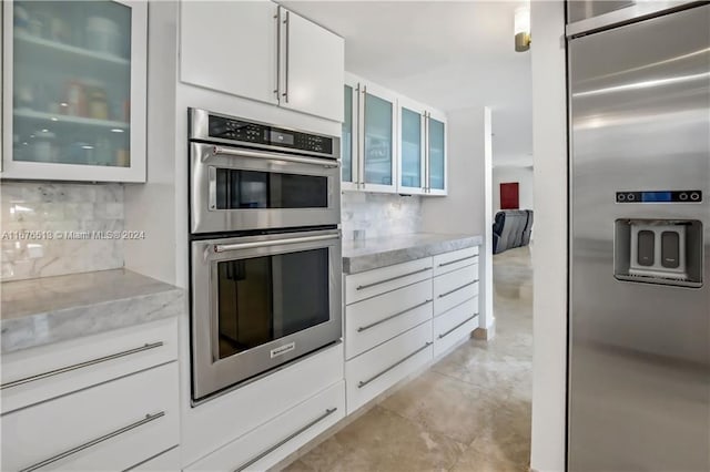 kitchen featuring decorative backsplash, white cabinets, stainless steel appliances, and light stone counters