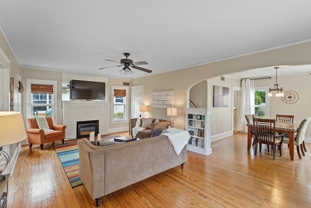 living room featuring ceiling fan with notable chandelier, a wealth of natural light, light wood-type flooring, and a fireplace