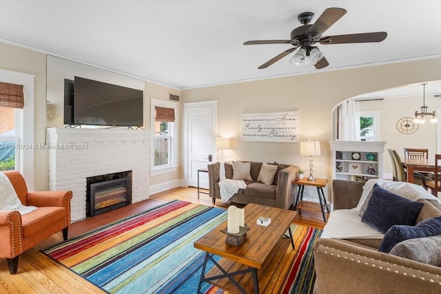 living room with crown molding, hardwood / wood-style floors, ceiling fan, and a brick fireplace