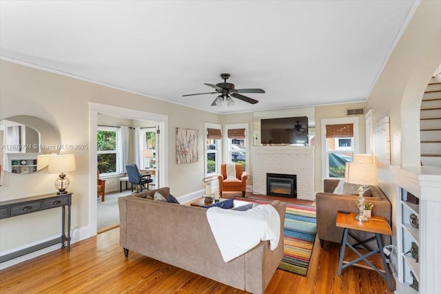 living room with light wood-style floors, a fireplace, visible vents, and ornamental molding